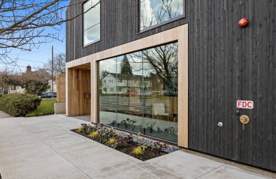 Exterior modern building with dark siding, large window, and landscaping. 1615 Wills Blvd #150, Portland, OR 97217. Spaces for rent by NWV Group.