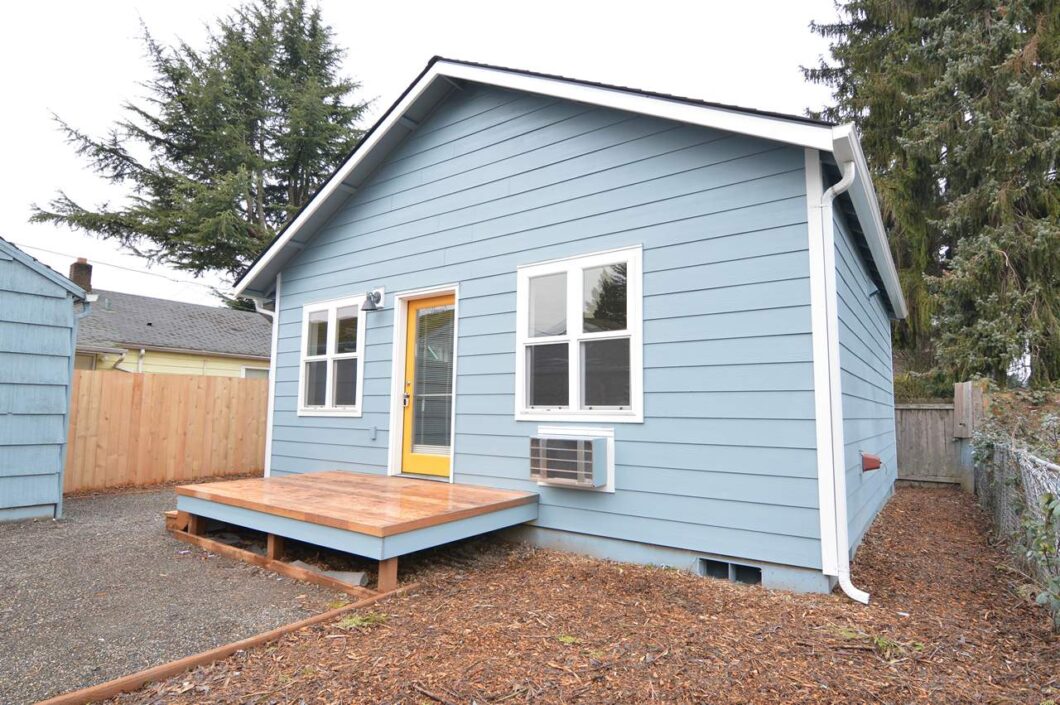 Blue house exterior with yellow door and small deck. 9572 N Calhoun Ave UNIT B, Portland, OR 97203. Spaces for rent by NWV Group.