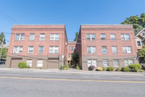 Exterior view of brick apartment building with parking. Spaces for rent by NWV Group. 1210 SE 20th Ave APT 103, Portland, OR 97214.